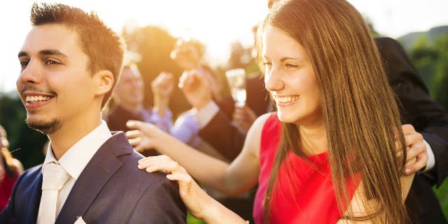 Woman in a red dress holds onto a suited man's shoulders in what appears to be a wedding celebration.