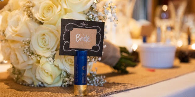 Blue shotgun shell placeholder for bride set on a table near bouquet.