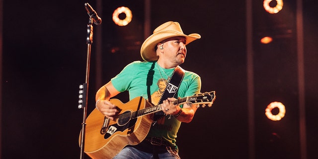 Jason Aldean wears a green T-shirt and holds his guitar on stage at CMAFest