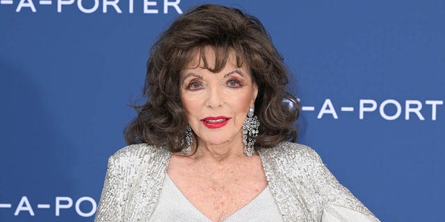 Joan Collins stands with her hand on hip on red carpet