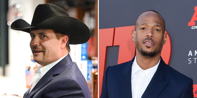 John Rich looks back at the camera wearing a black cowboy hat and navy suit split Marlon Wayans in a navy suit on the "Air" red carpet