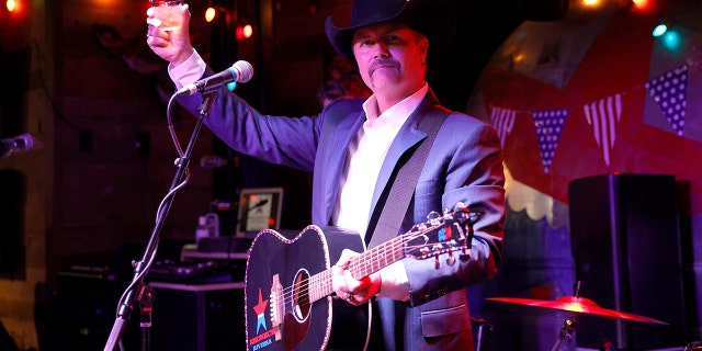 John Rich holds whiskey glass in the air with guitar strung around his neck at Nashville bar