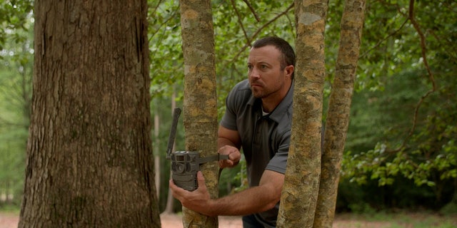 Josh Highlander attaches a trail camera to a tree