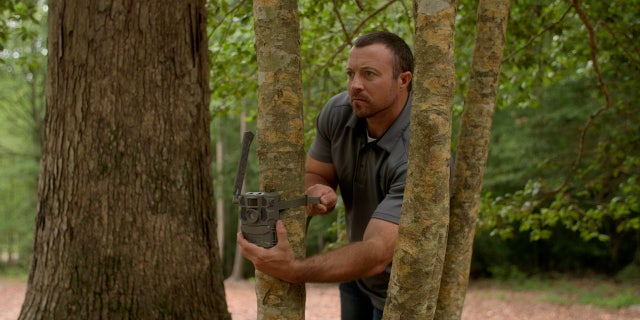 Josh Highlander attaches a trail camera to a tree