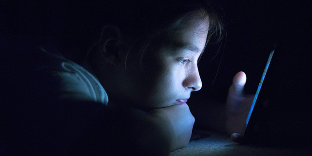 Teenager sending email from smart phone in her bed,