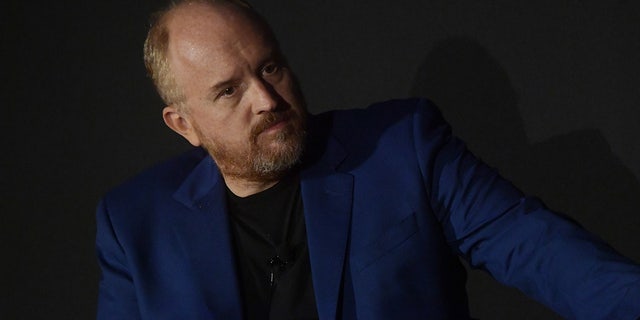 Comedian Louis C.K. wears blue blazer and black shirt on stage during panel discussion