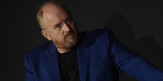 Comedian Louis C.K. wears blue blazer and black shirt on stage during panel discussion