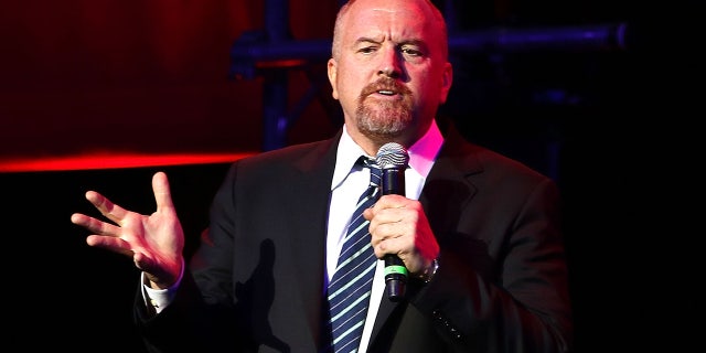 Louis C.K. holds a microphone while performing on stage