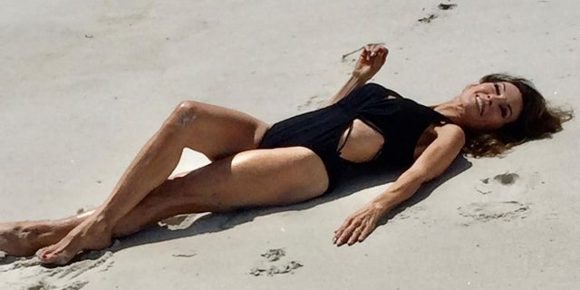 Susan Lucci laying on the beach in a black swimsuit