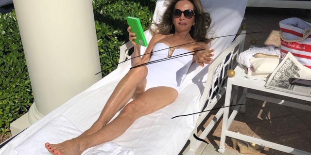 Susan Lucci lounging on a beach chairin a white one-piece 