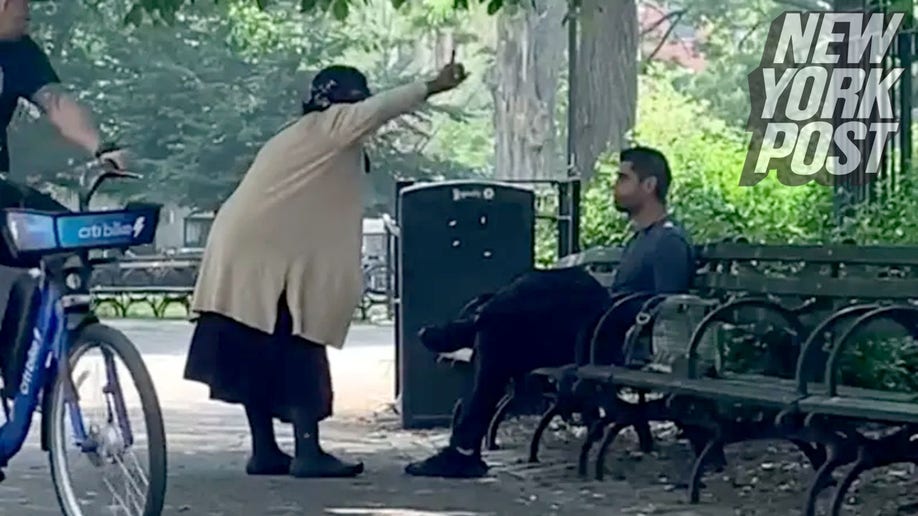 Woman gestures at man seated on park bench