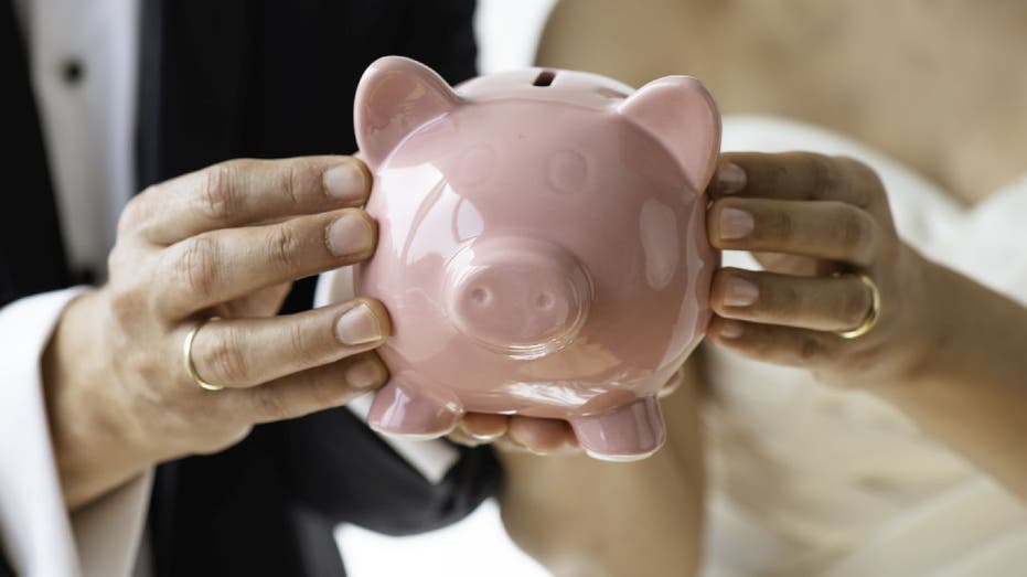 Bride and groom hold pink piggybank.