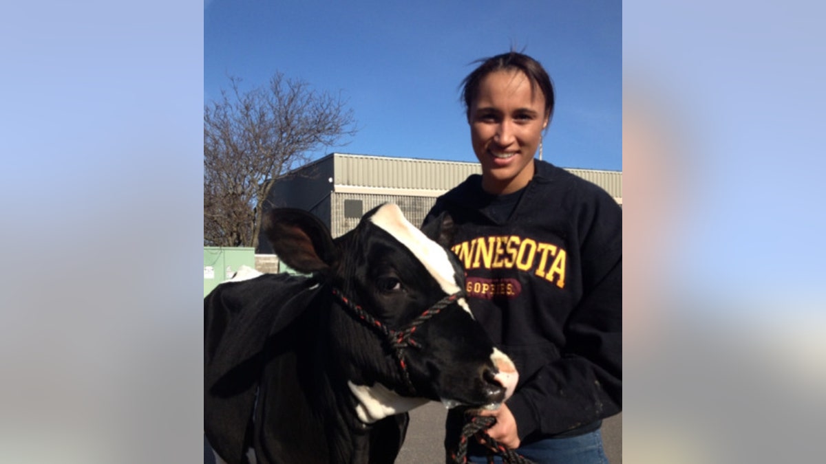 Danicka Bergeson poses next to a cow, wearing a University of Minnesota sweatshirt