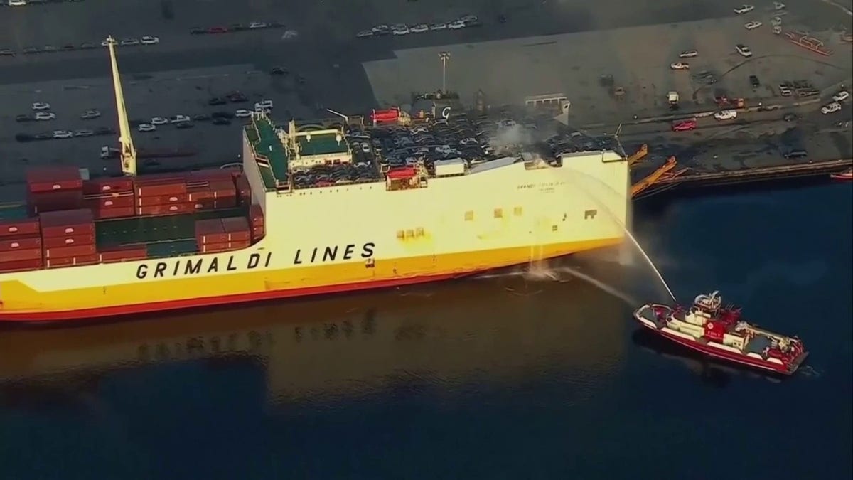 firefighter boat spraying deck of cargo ship with water