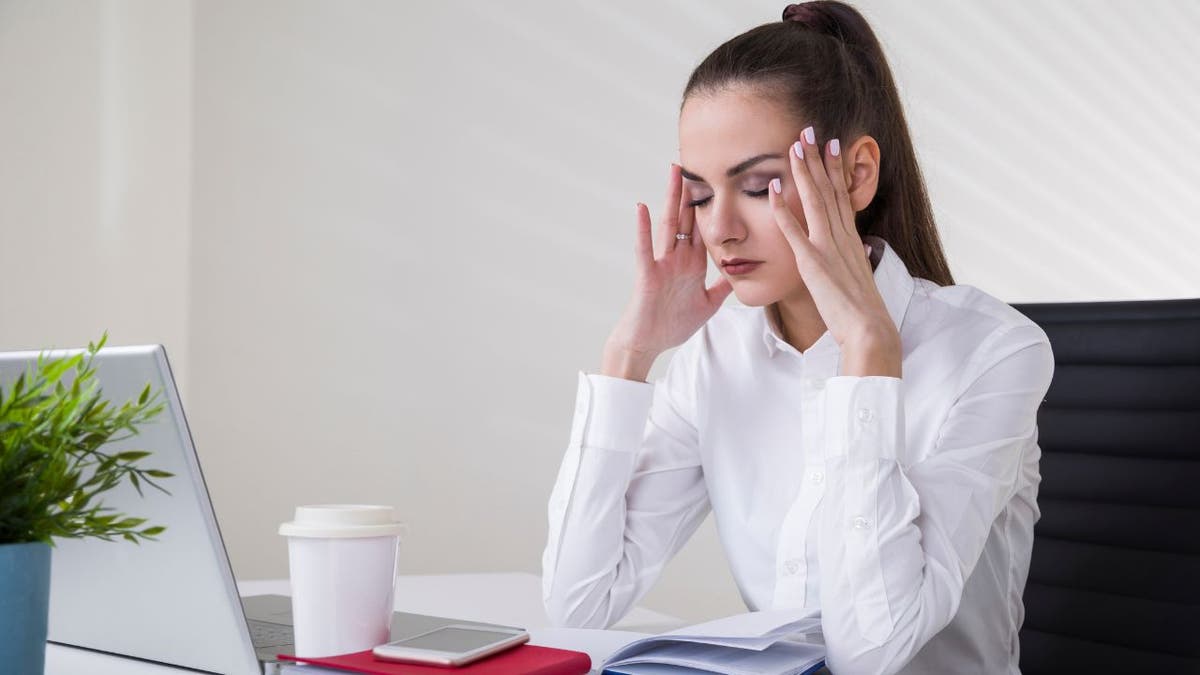 Stressed out woman holds her head as she works on computer
