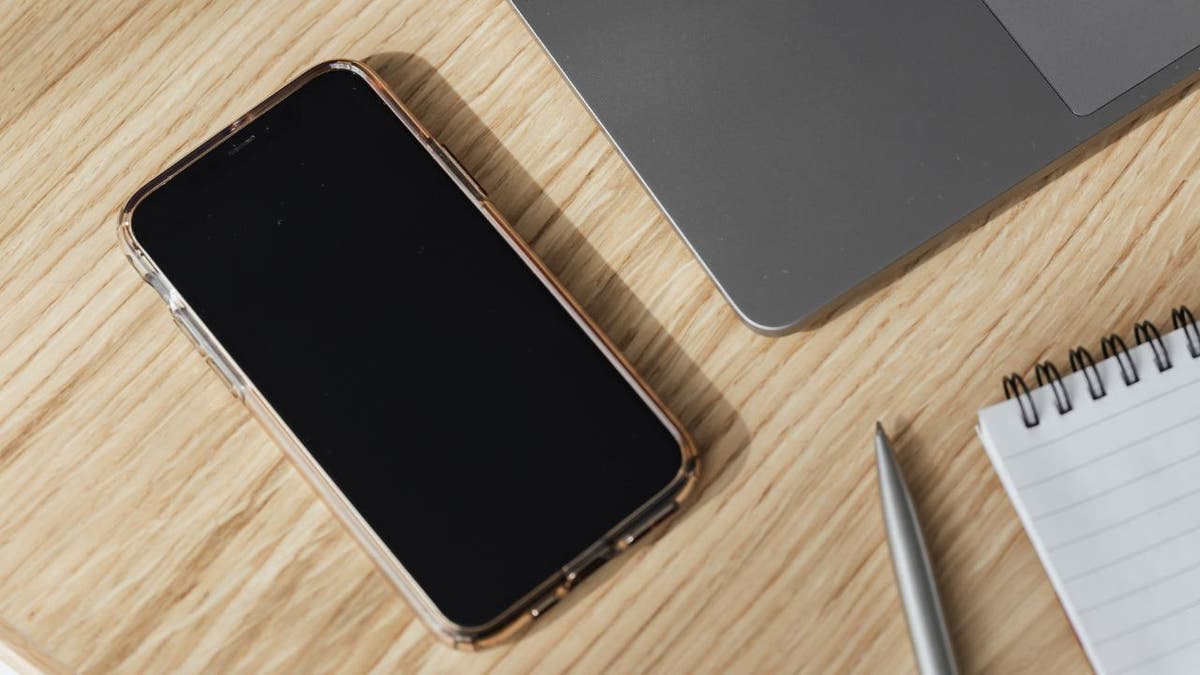 iPhone with dark screen on desk with laptop and notepad 