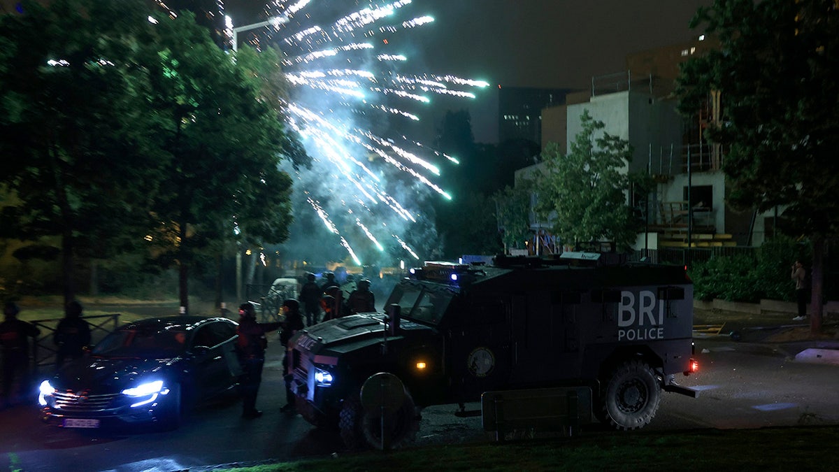Fireworks explode in the sky above armored vehicles amid France riots