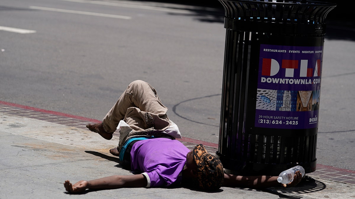 A homeless person lies on the sidewalk