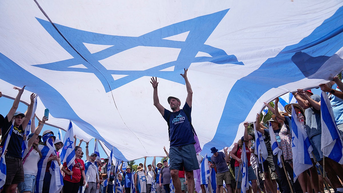 Large Israeli flag above a group of protesters