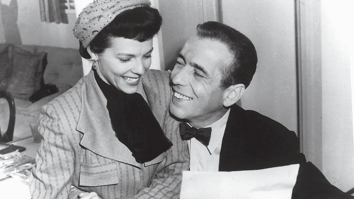 Verita Thompson sitting on Humphrey Bogarts lap while they read a letter.