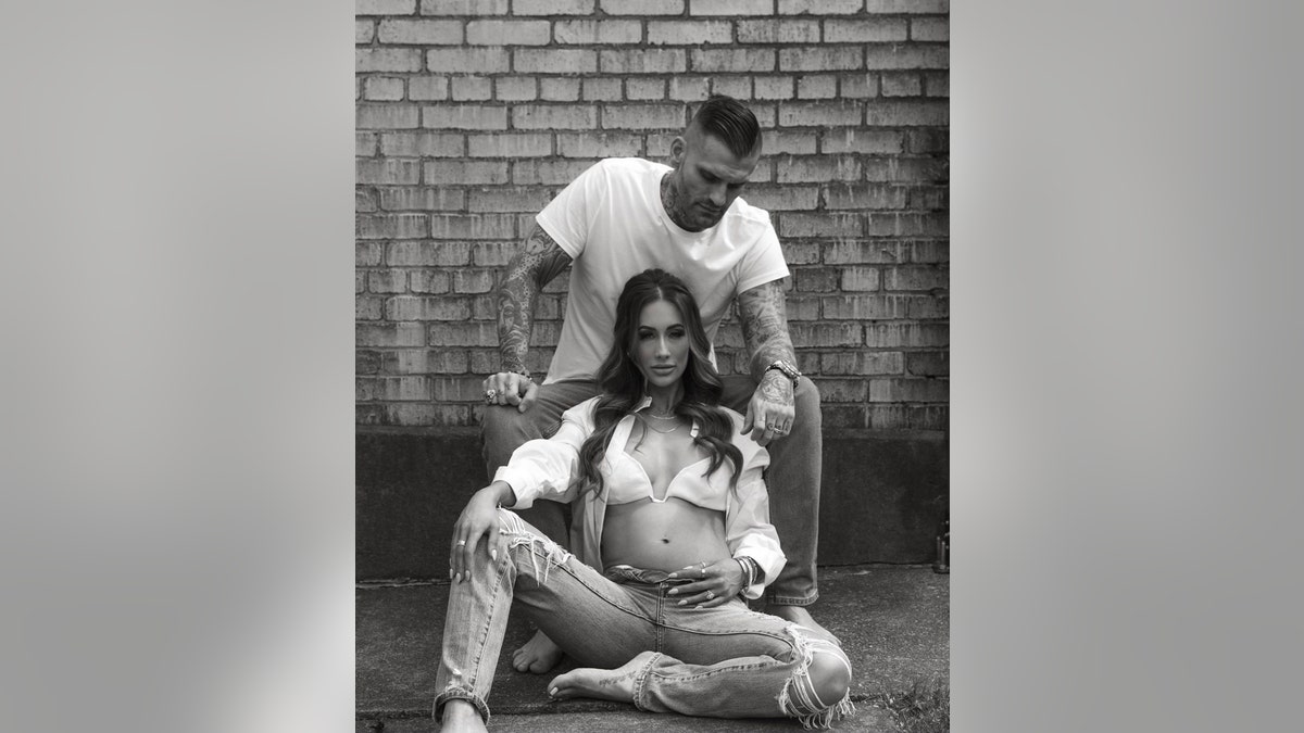 Leah Van Dale wearing a white bikini top with an open white blouse and sleeves sitting down with Matt Polinsky sitting above her wearing a white shirt and jeans in a black and white photo