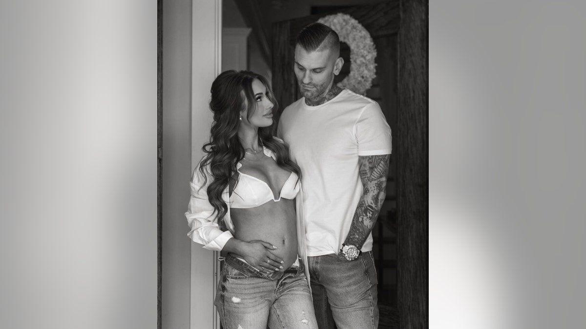 A black and white photo of Leah Van Dale caressing her baby bump in a white bikini top and jeans next to Matt Polinsky in a white shirt and jeans