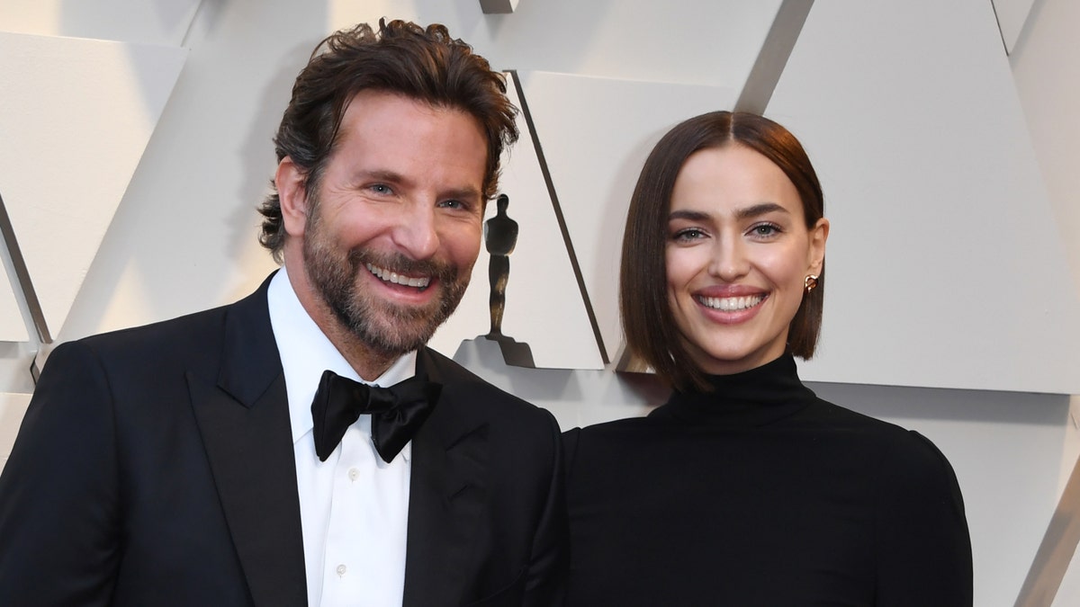 Bradley Cooper in a traditional tux and Irina Shayk in a black turtleneck dress smiles at the Oscars