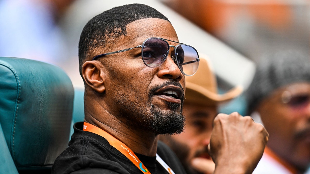 Jamie Foxx pumps his fist in the air while watching tennis