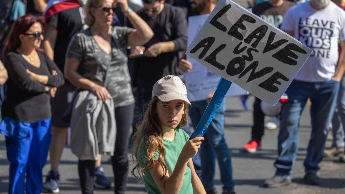 A girl holds a sign reading "Leave Us Alone"