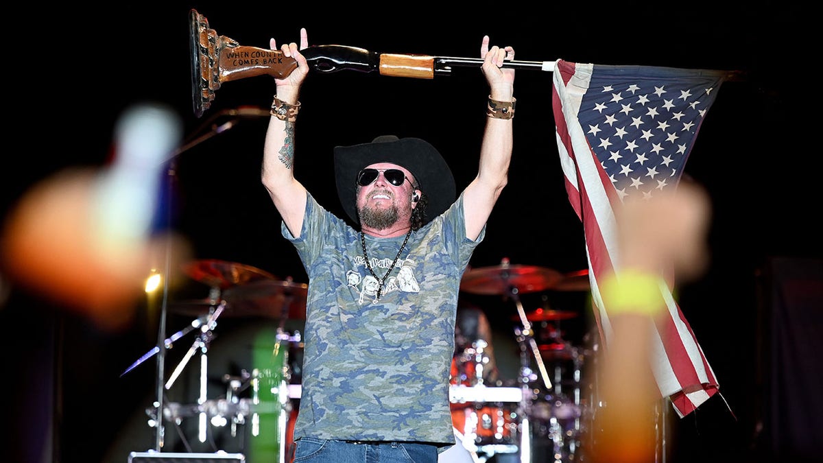Colt Ford holds up a mic stand draped with an American flag