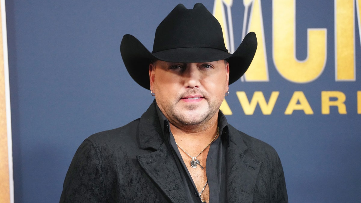 Jason Aldean smiles in black on the carpet