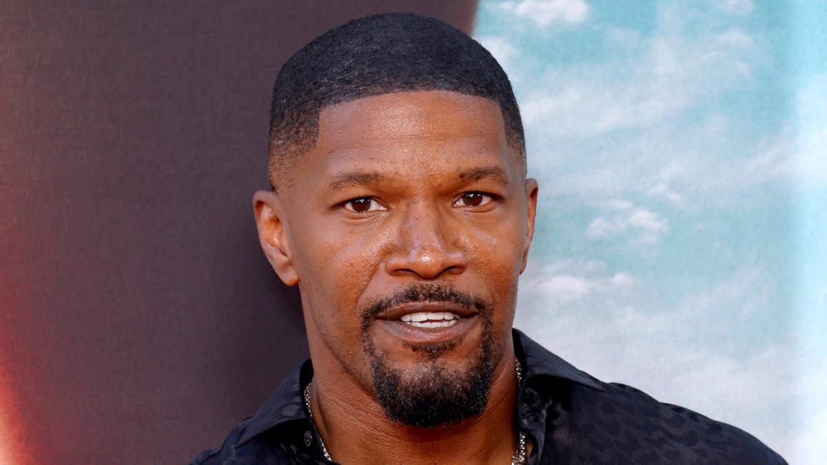 Jamie Foxx smiles on the red carpet in a black shirt