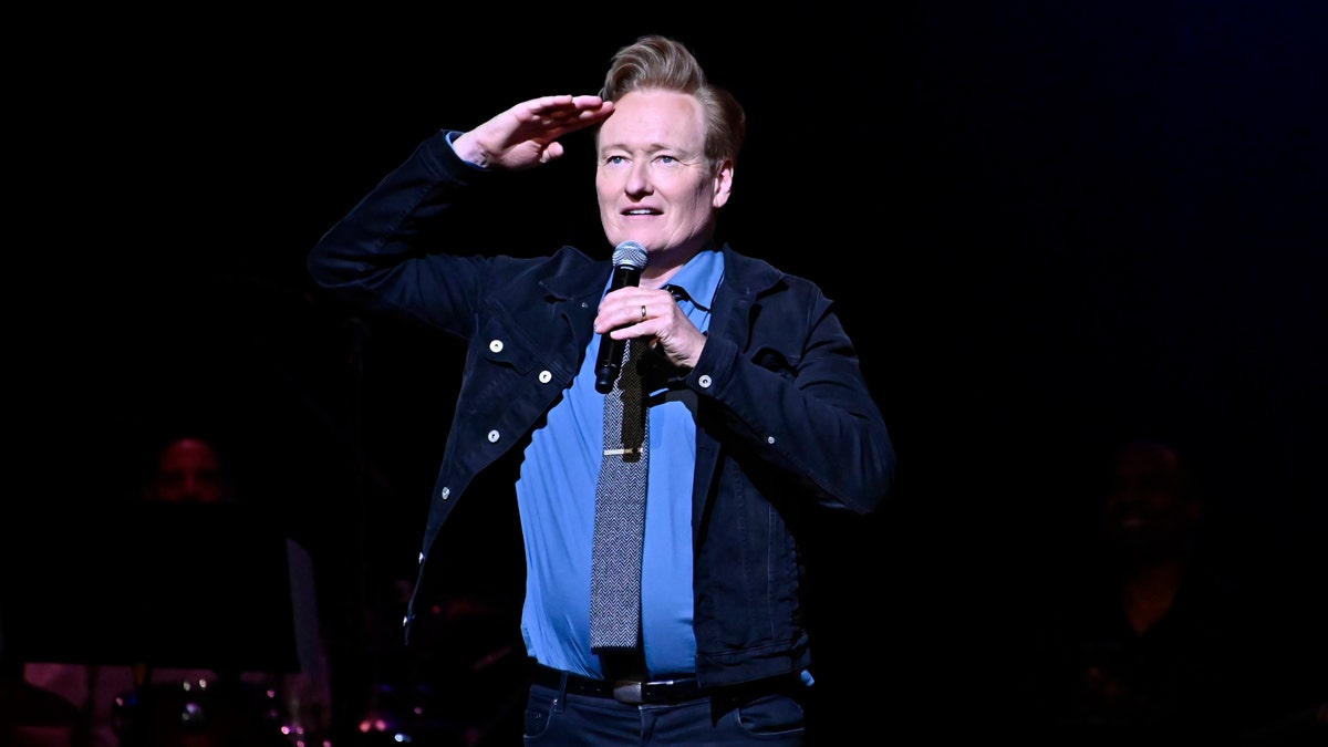 Conan O'Brien salutes the crowd on stage while holding a microphone