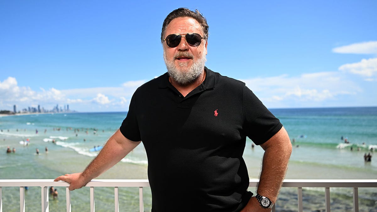 Russell Crowe poses for a photo in front of a beach