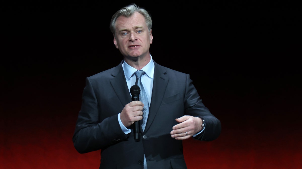 Christopher Nolan speaks on stage and holds a microphone while promoting his film "Oppenheimer" at CinemaCon in Las Vegas