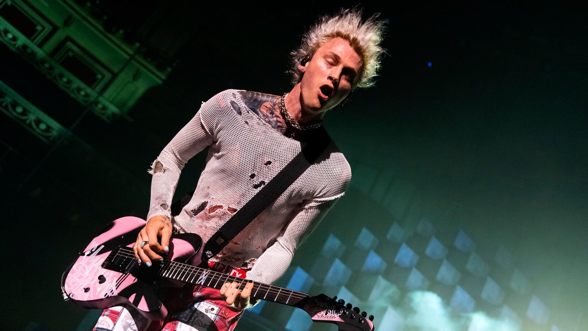 Machine Gun Kelly looks down and plays his guitar in London