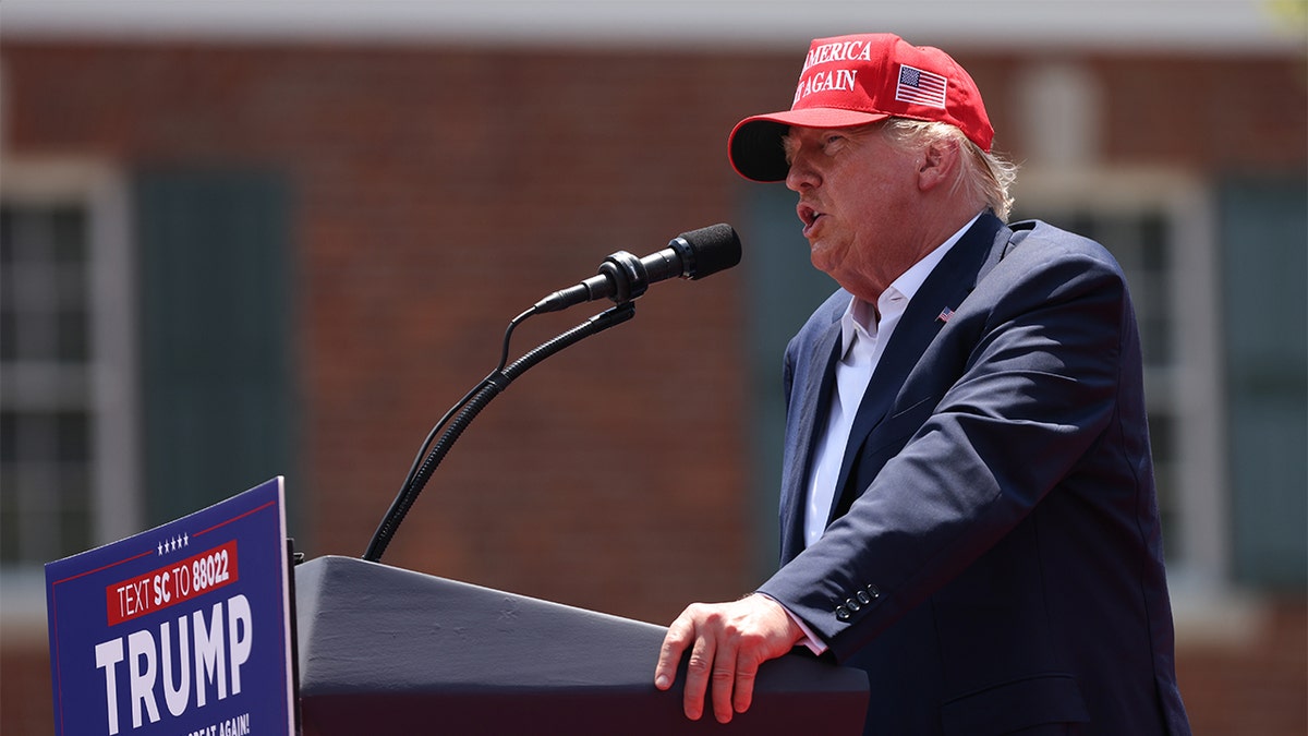 Donald Trump con sombrero rojo MAGA en el atril