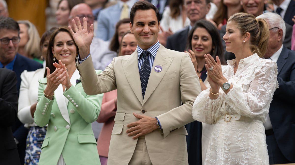 Roger Federer waves his hand as he is the recipient of applause at Wimbledon next to wife Mirka and Kate Middeton