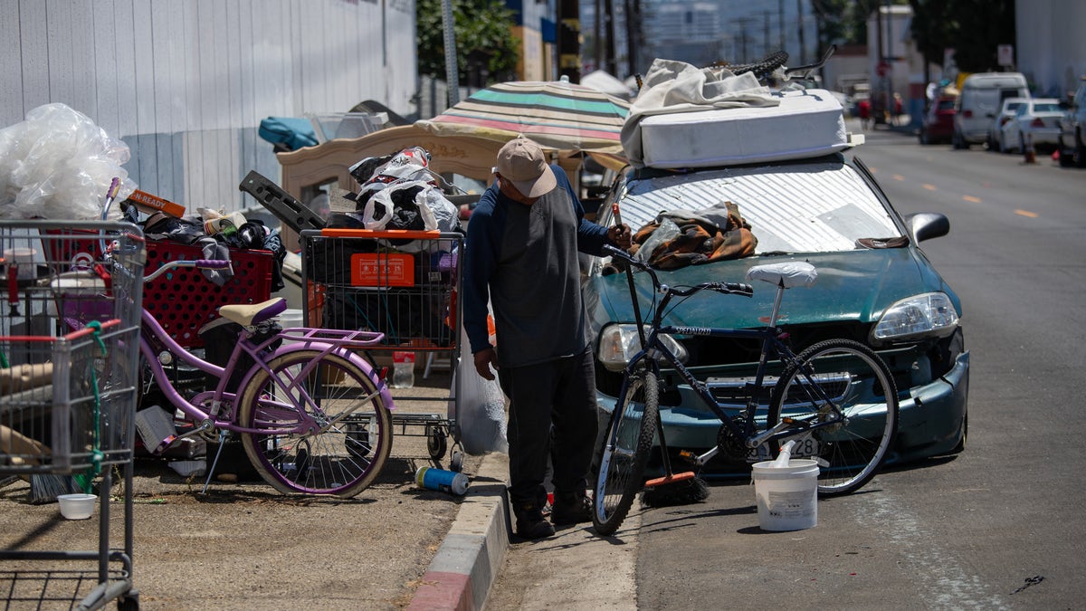 A homeless man sweeps up around a sidewalk encampment on Deering Avenue on July 10, 2023 in Canoga Park, California.