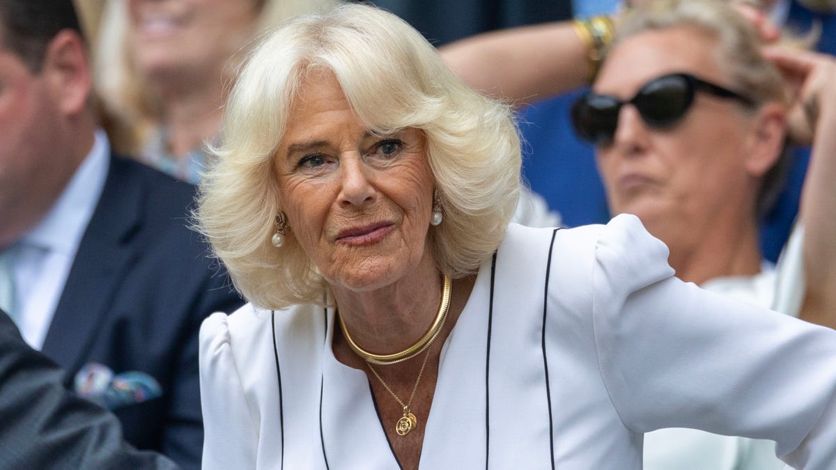 Queen Camilla in a white suit sits front row at Wimbledon and looks to her left