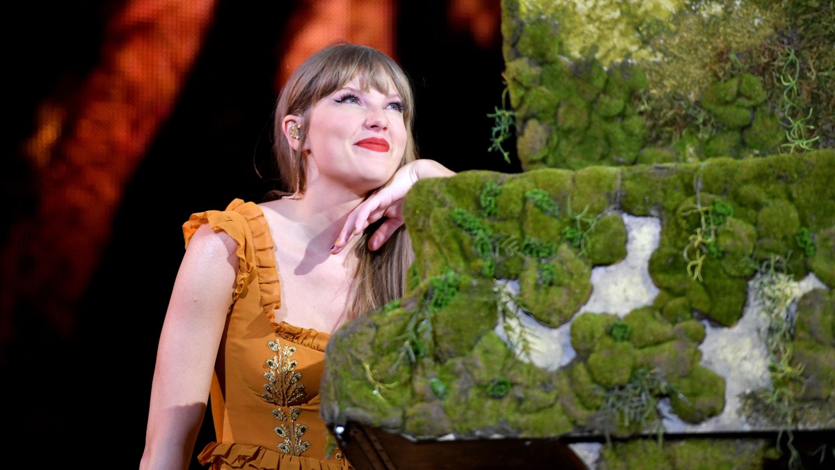 Taylor Swift looks up leaning against her moss covered piano playing in Denver