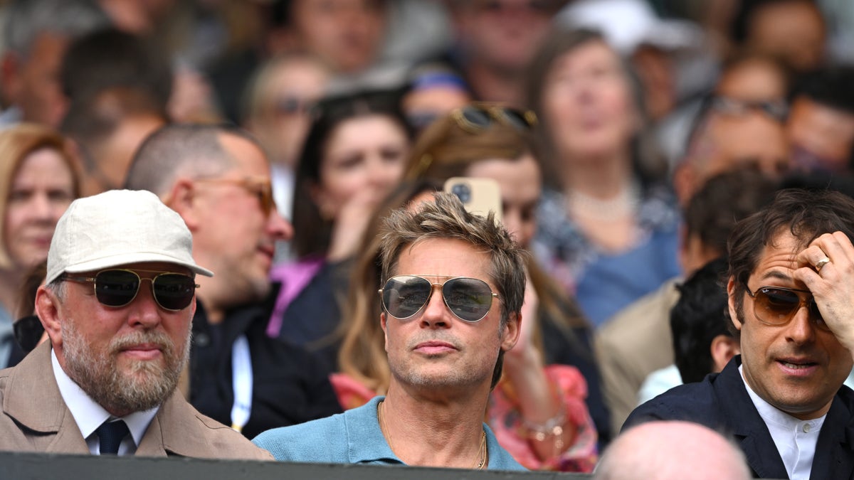 Brad Pitt wearing sunglasses and blue shirt in the stands at Wimbledon.