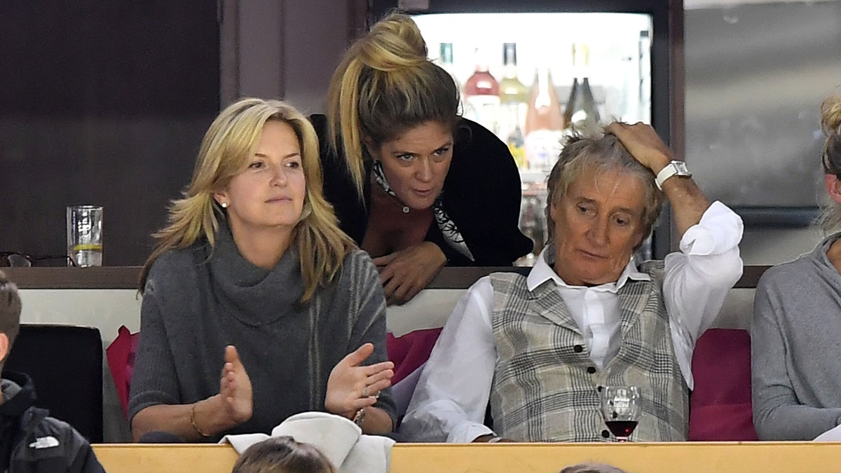 Rod Stewart sits next to Penny Lancaster as ex-wife Rachel Hunter leans over