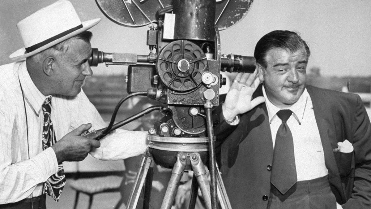 Lou Costello holds ear to camera aboard the Queen Elizabeth.