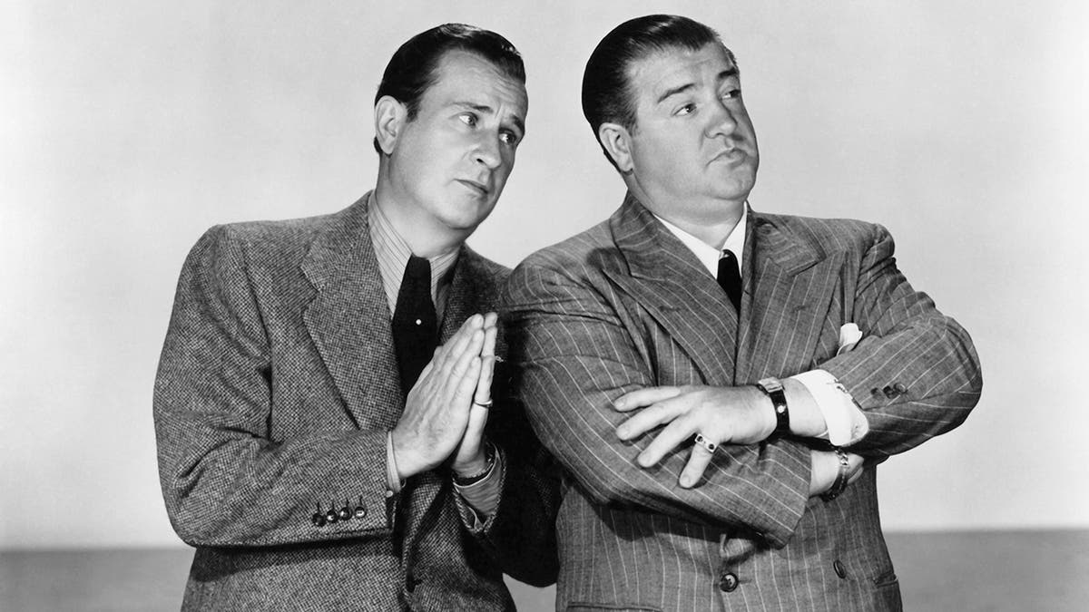 Bud Abbott wearing a suit with praying hands as Lou Costello in a suit and tie looks away