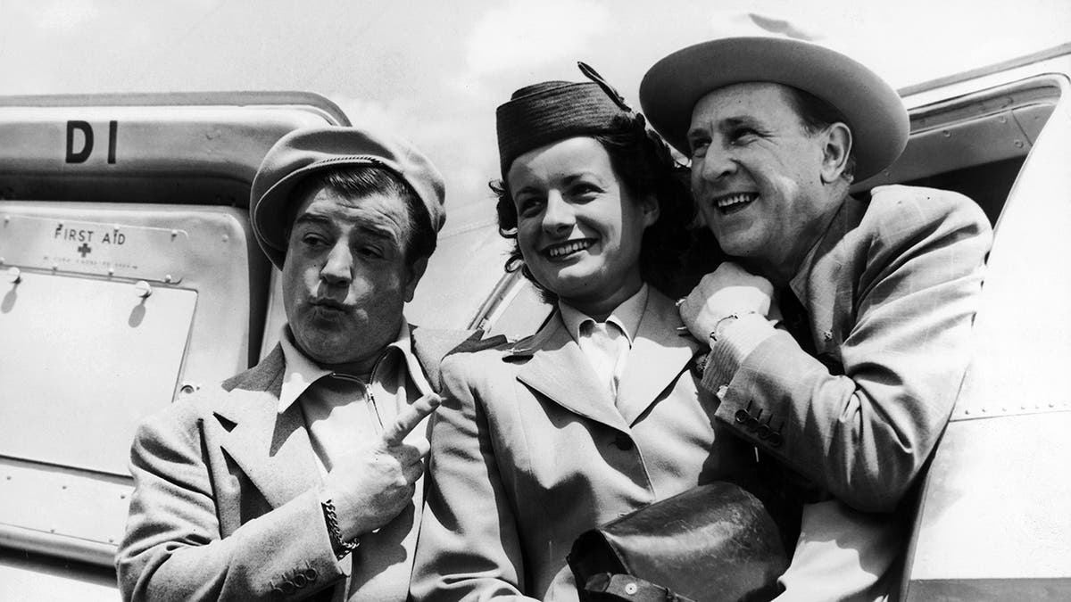 Lou Costello pointing at a servicewoman with Bud Abbott leaning in and smiling