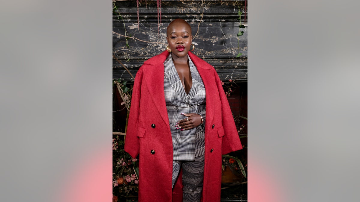 Achieng Agutu wearing a grey plaid suit with a red coat