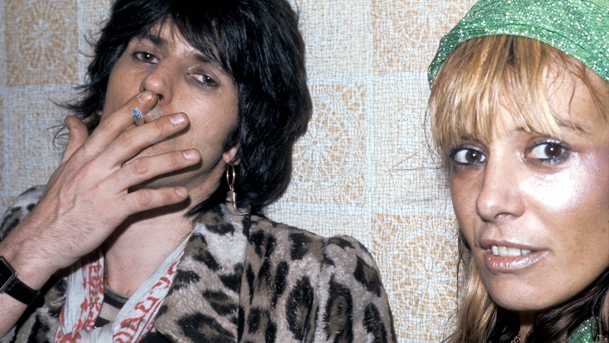 Keith Richards in an animal-print coat smoking a cigarette next to Anita Pallenberg