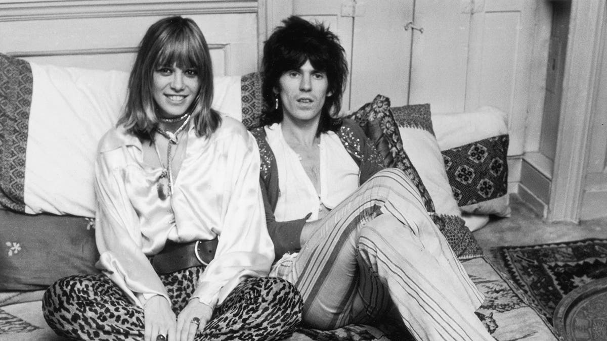 Anita Pallenberg and Keith Richards wearing white blouses and striped pants sitting in bed