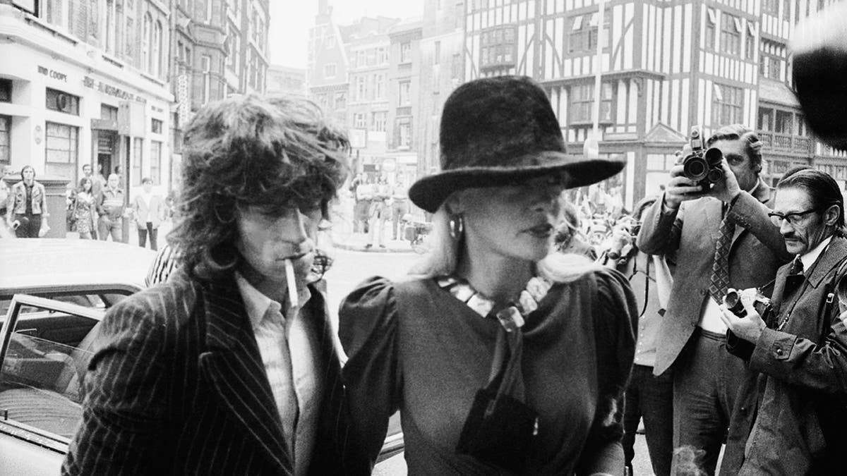 Anita Pallenberg walking ahead of Keith Richards wearing a hat that covers her face